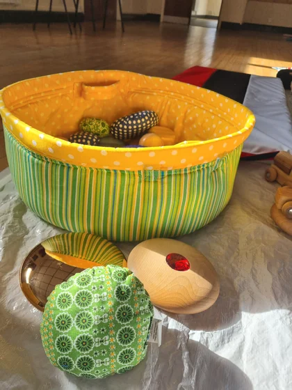 A bright yellow sensory basket with tactile cushions and wooden play resources