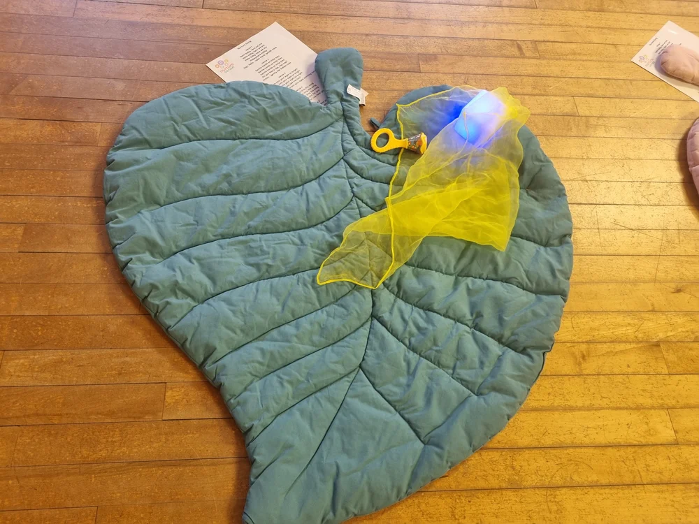A soft leaf-shaped mat set up with a yellow sensory scarf, rattle and glowing light cube